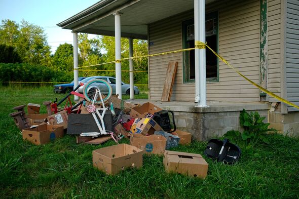 Police tape surrounds a home and debris is seen on the front lawn, including baby carrier, where authorities say they removed 16